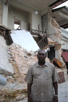 Haitian credit union chair stands beside wrecked building