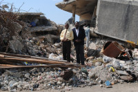 El Presidente del Consejo de KOTELAM Jean Hubert Lindor (izquierda) y el Director Gervase Michel, de pie encima de los escombros de lo que antes fue la sucursal de Magloire Ambroise en el centro de Puerto Príncipe.